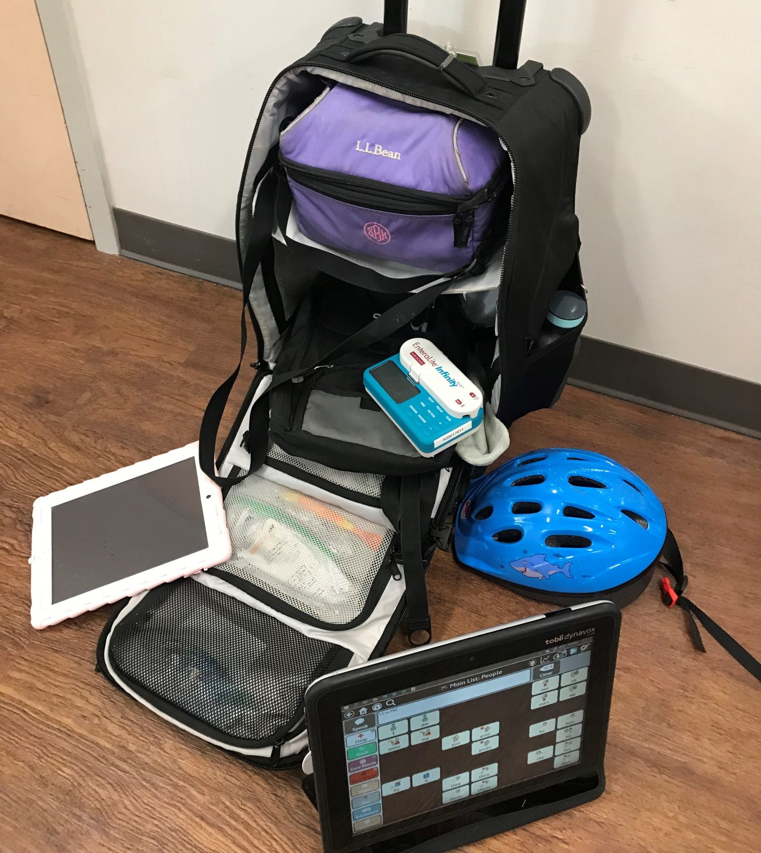 Luggage packed with emergency items including helmet, speech device, and enteral feeding pump